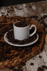 close up of roasted coffee beans inside a classic elegant white espresso mug on a whisper tablecloth and a rustic table 