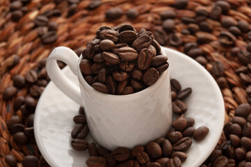 close up of roasted coffee beans inside a classic elegant white espresso mug on a whisper...