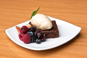 Chocolate cake with walnut ice cream, red berries and fig served on white plate on wooden background