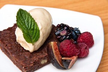 Chocolate cake with walnut ice cream, red berries and fig served on white plate on wooden background