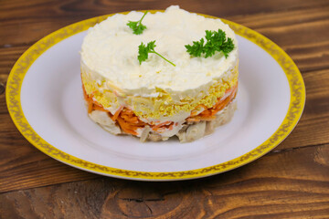 Tasty layered salad with chicken, carrot, eggs, cheese and mayonnaise on wooden table