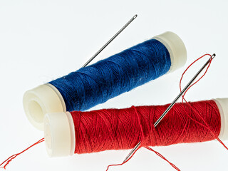 Zwei Spulen mit Nähgarn in rot und blau mit zwei Nähnadeln freigestellt auf weißem Hintergrund