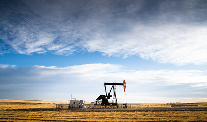 An industrial oil pump jack working on farm land under a morning sky in Rocky View County Alberta Canada.
