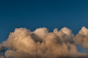 cumulus cloud illuminated by the evening light, floating gently on the horizon under a blue sky.