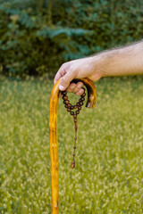 Elderly religious muslim man holding walking stick and a string of rosary beads while praying in outdoors. Old man with prayer-beads walking outside.