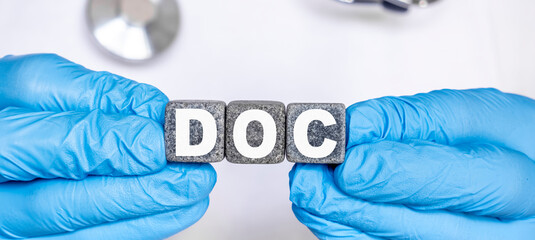 DOC - word from stone blocks with letters holding by a doctor's hands in medical protective gloves