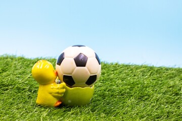 Fototapeta premium Soccer Easter Holiday with chicken holding ball on green grass blue sky background