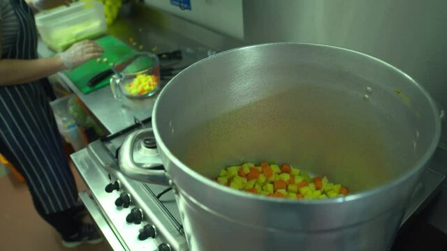 Chef prepares vegetable for large soup broth stock pot on kitchen stove