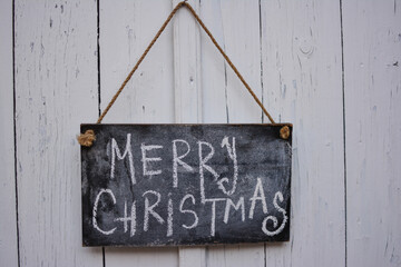 Merry Christmas text handwritten on vintage Christmas wooden sign, hung on a white wooden rustic door. Greeting card, modern seasons greetings. Happy holidays