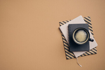 Cup of coffee and stack of paper notebooks on pastel brown background. Business, coffee break concept top view.