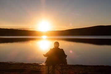 Back view of a man sitting in a chair and admiring the sunset at the Temiscouata national park, Canada