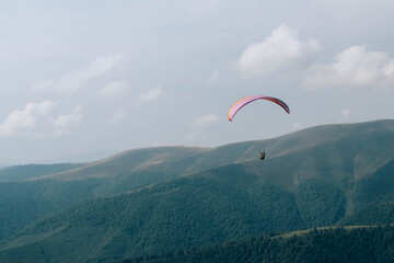 Paraglide silhouette flying over Carpathian peaks and clouds.