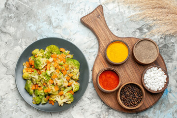 Above view of healthy vegetable salad different spices and cutting board on white background