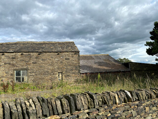 Deserted farm buildings, near a dry stone wall, with heavy rain clouds above in, Bradford,...