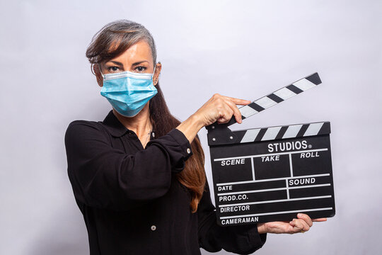 Mulher de máscara protetora contra a pandemia com claquete na mão em fundo branco