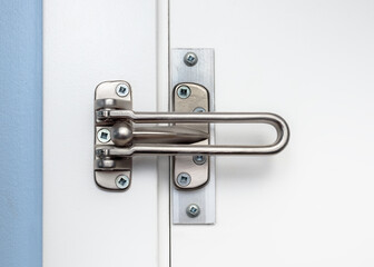 Naklejka premium Door lock guard installed on white closed door, front view. Also known as hinged bar lock or security door guard. Home safety hardware limiting door openings in residences. Selective focus.