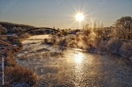 Fototapete 霜で凍り付いた川岸の木々 川から立ち上る朝靄 輝く太陽 田舎の町の冬の朝の風景 Doutou Life