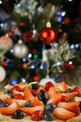 Fototapeta na wymiar Christmas mood dessert, delicious fruit cake with strawberries and cranberries in front of christmas tree
