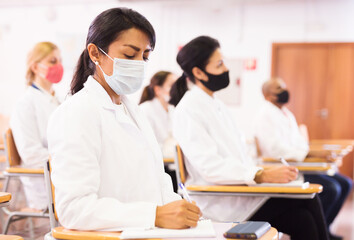 Fototapeta premium Portrait of young adult female doctor attentively listening to lecture with colleagues, medical conference during coronavirus pandemic