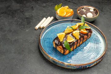 Soft cake decorated with lemon and chocolate on tray and other cookies dark background