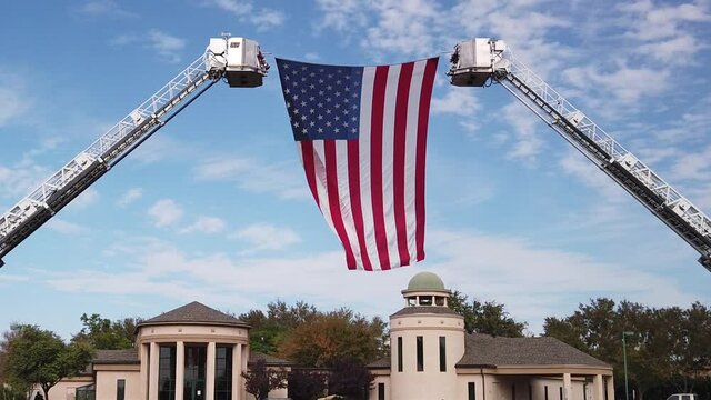 A large American Flag is suspended between two ladders waves over several mortuary buildings.
