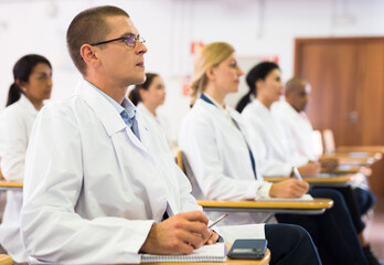 Obraz premium Portrait of male doctor attentively listening to lecture with colleagues at medical conference