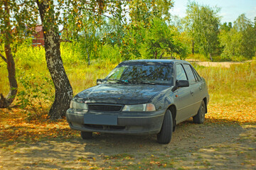 A dark passenger sedan stands in a clearing in the forest in summer close-up. Blurry focus