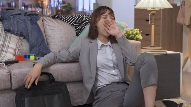 portrait asian female in business suit yawning and fainted with exhaustion, hand propping head on sofa.