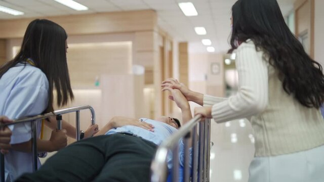 Group Professional Asian doctor with surgeon and patient relative moving unconscious male patient on stretcher through hospital lobby to operating room. Medical treatment healthcare service concept.