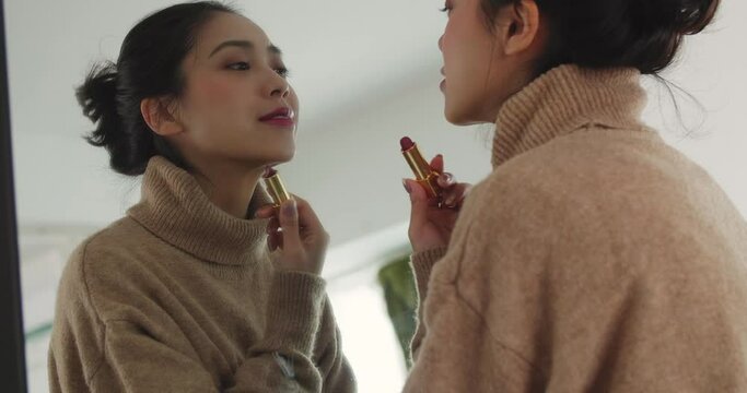 Young Asian girl applying lipstick in front of the mirror makeup and looking at herself in the mirror very happy Full of confidence