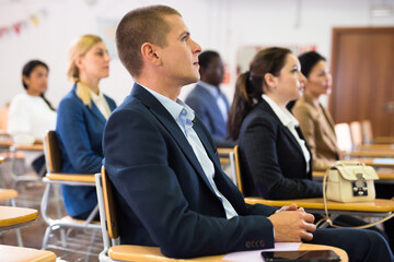 Young confident man sitting and listening speaker at business conference