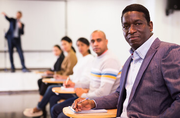 Young confident man sitting and listening speaker at business conference