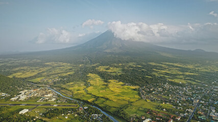 Volcano erupt at countryside cityscape aerial. Urban cottages with traffic road at green valley. Legazpi city at Mayon mount landscape, Philippines, Asia. Cinematic tourist attraction at mist haze