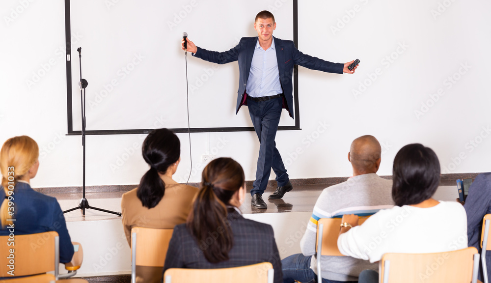 Wall mural Young emotional male motivation coach giving speech from speaker stage