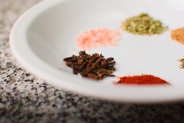 Cloves on a white dish over a granite kitchen countertop. Extreme close up.
