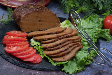 Vegan seitan roast ham slices with tomato slices on lettuce leaves on slate plate