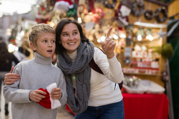 Happy tween boy choosing Xmas decorations and gifts on street fair with his loving mother..