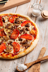 Side view on minced meat pizza with mushrooms and tomatoes on the wooden table