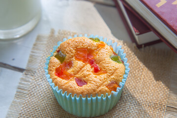 High angle view a sweet fruit Mamon cup cake on a white table next to a cup of milk and books