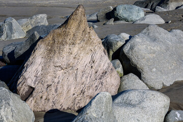 Large rocks on a wet sandy beach, purple triangle shaped rock in middle of smooth gray rocks
