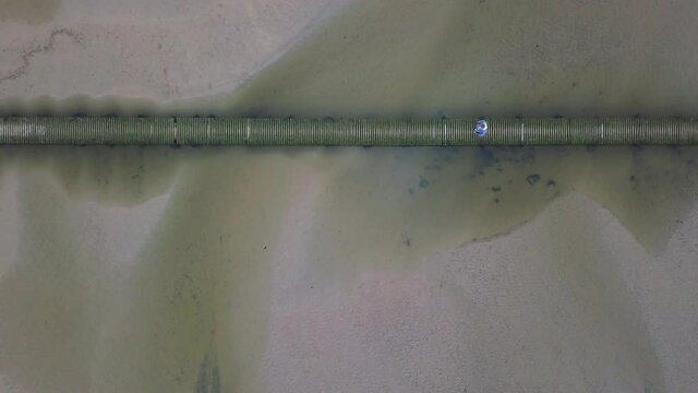 Man Walking On Wooden Bridge Across Sandy River Gannel In Newquay, UK - aerial top-down