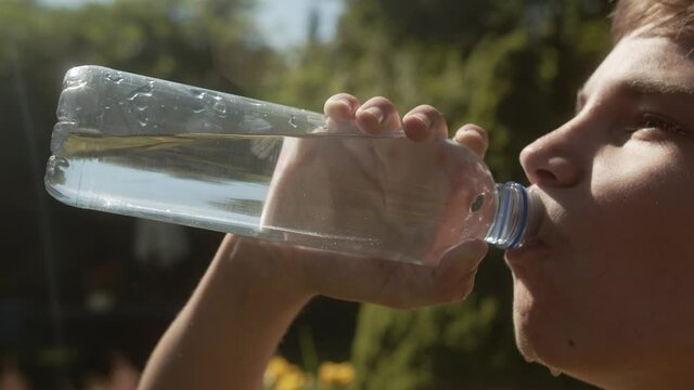 Boy drinking cold water from a plastic water bottle on a hot summer day.