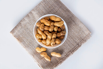 Unpeeled peanuts in white bowl on sacking. Treats for Indian Canadian Punjabi holiday festival of Lohri
