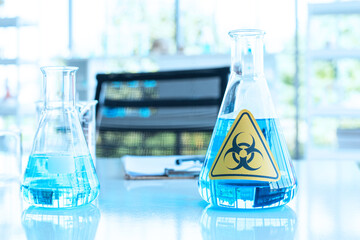 Erlenmeyer Flask and blue fluid inside with panoramic caution danger signage on test lap table.