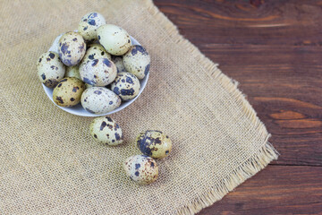 Quail eggs lie in a pile on the burlap on an old wooden background.