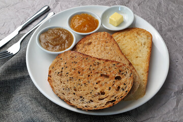 Whole grains bread with seeds served with kaya, butter and jam on a white plate.