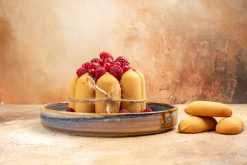 Horizontal view of freshly baked soft cake with fruits and biscuits on mixed color table