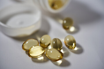 Omega-3 gel capsules with fish oil are poured from a bottle on a white background