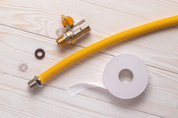 Gas stopcock, yellow flexible hose and accessories for connection to gas line. On white wooden...