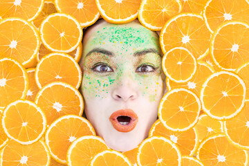 Female portrait with oranges close-up. A woman with bright makeup in oranges. Beauty portrait. the emotion of surprise.